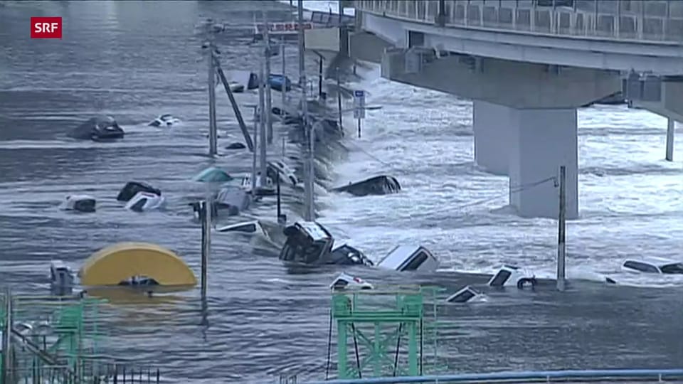 Tsunami reisst in der Küstenstadt Sendai Autos und Häuser mit